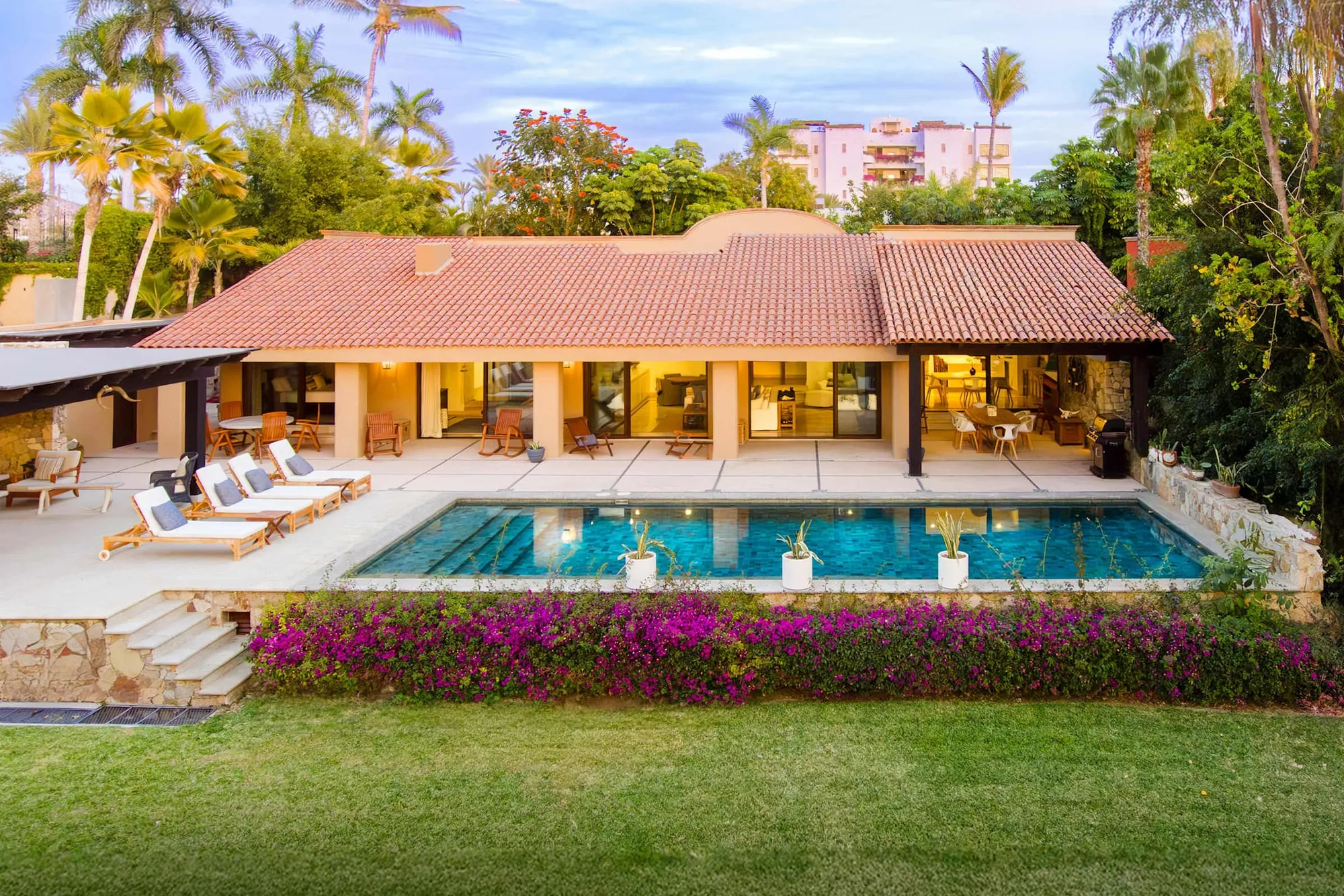 The Cabo Real house at dusk, its pool lit and bougainvillea along the garden