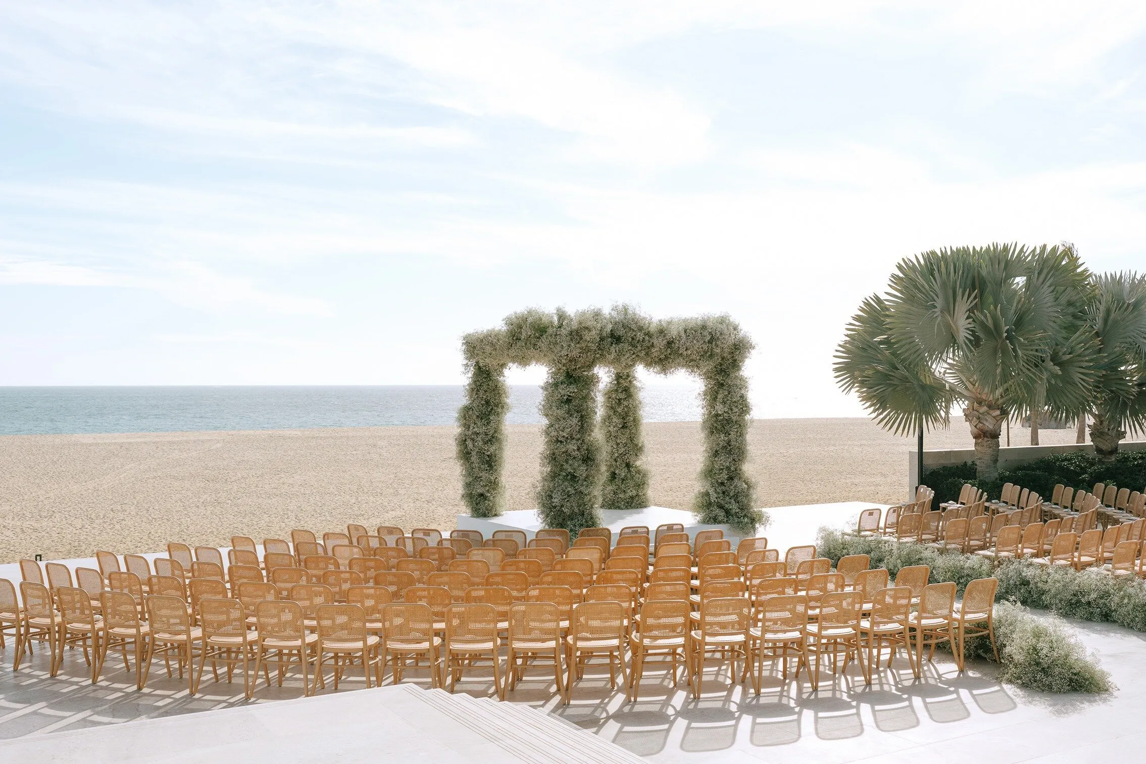 A beach ceremony at Nobu Los Cabos, chairs curved around a tall pale arch