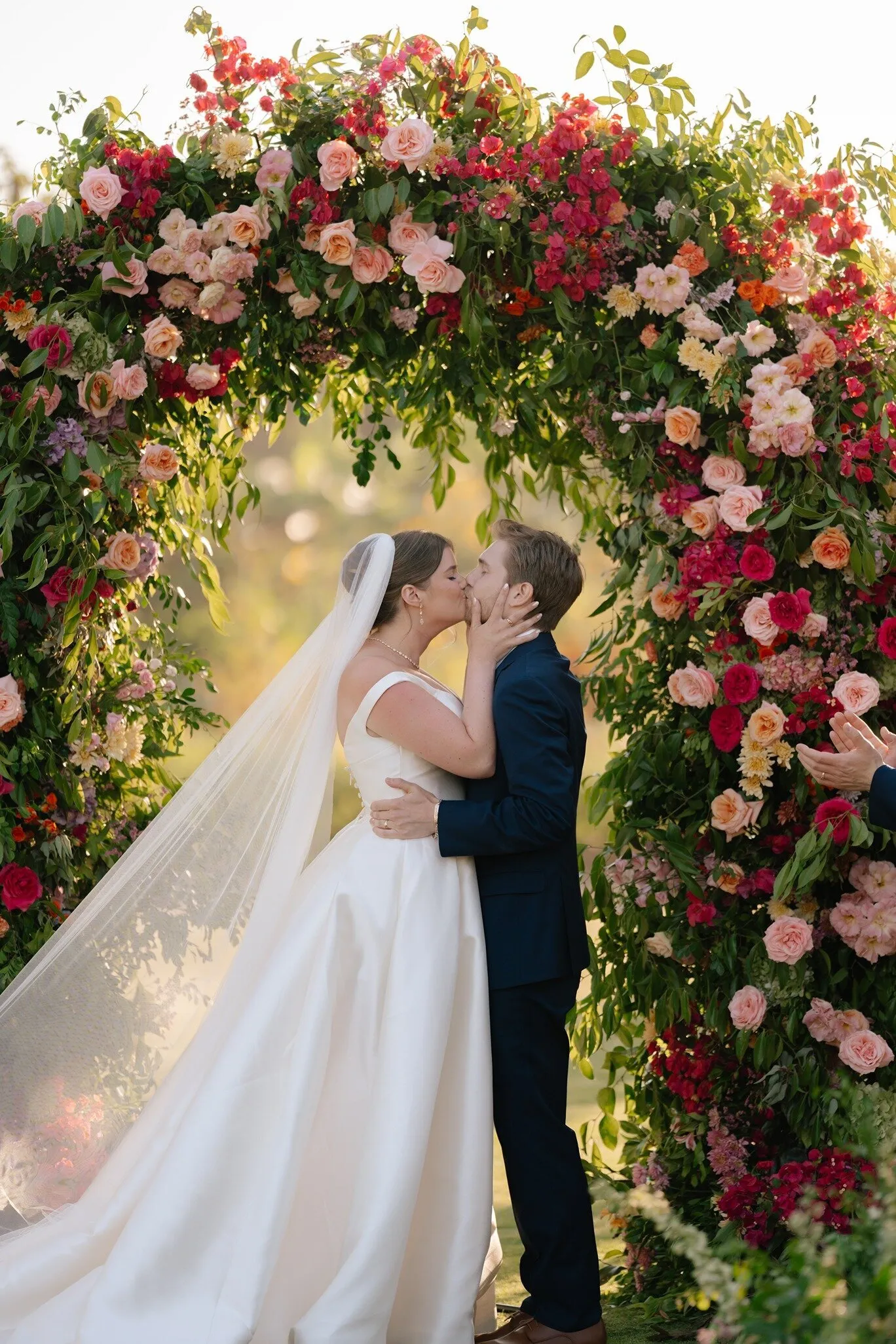 A couple kissing under a dense floral arch at Flora Farms