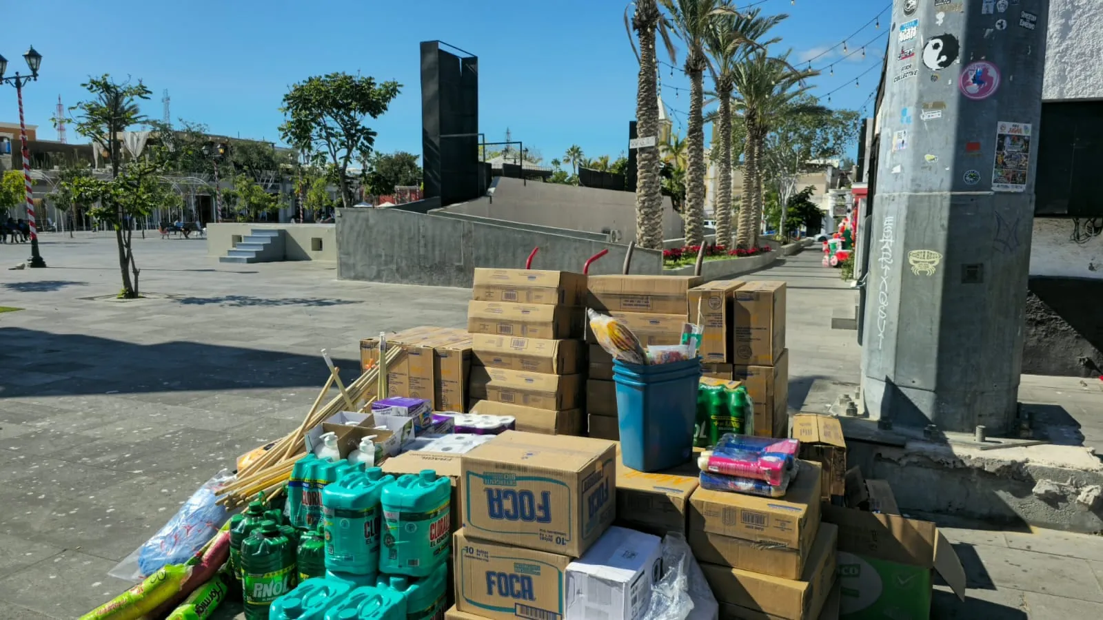 A delivery of cleaning supplies stacked on the plaza in San José del Cabo, palms and the church behind