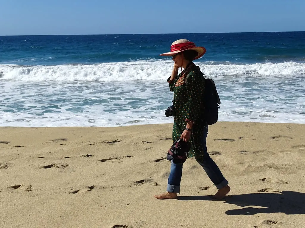 A woman in a red sun hat walking the sand at Cerritos beach as the surf breaks