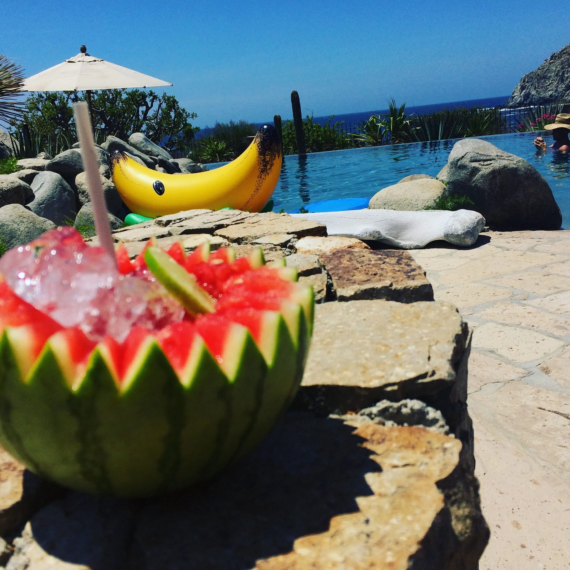 A carved watermelon bowl filled with ice and drinks beside a villa pool