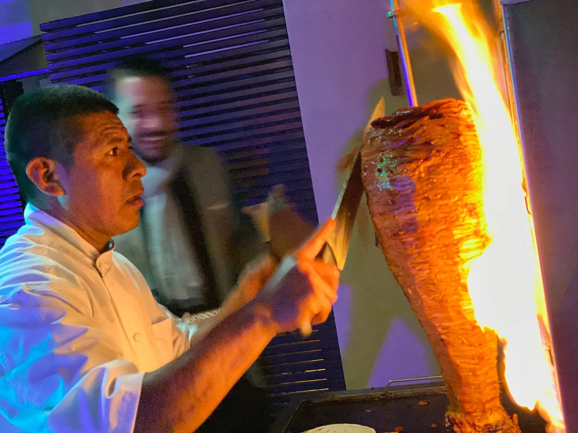 Their taquero carving tacos al pastor from the flaming trompo at a live station