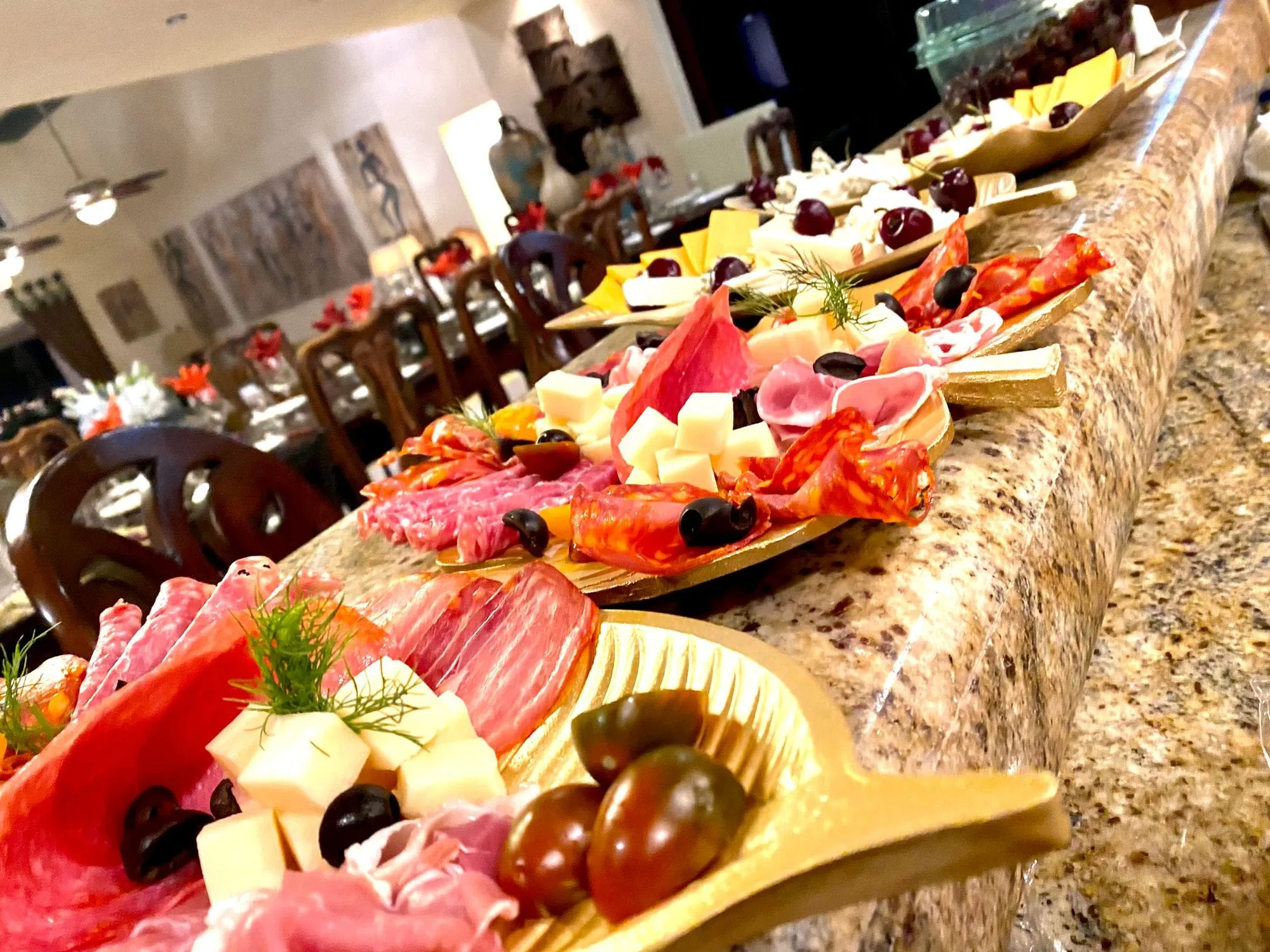Charcuterie and cheese boards laid the length of a private villa's kitchen island, the dining table set behind