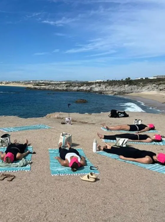 A group lying in savasana on towels on the sand, the bay behind them