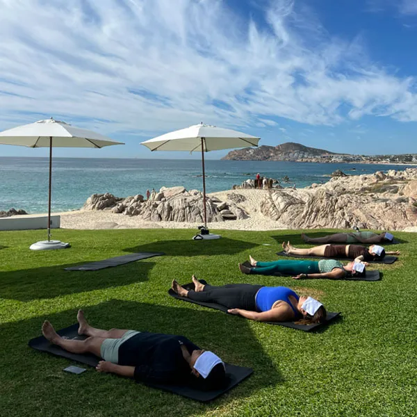 A group class on a lawn above the sea, mats laid out under white umbrellas