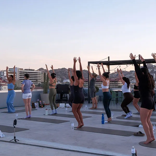 A rooftop class at golden hour, two dozen people with their arms raised