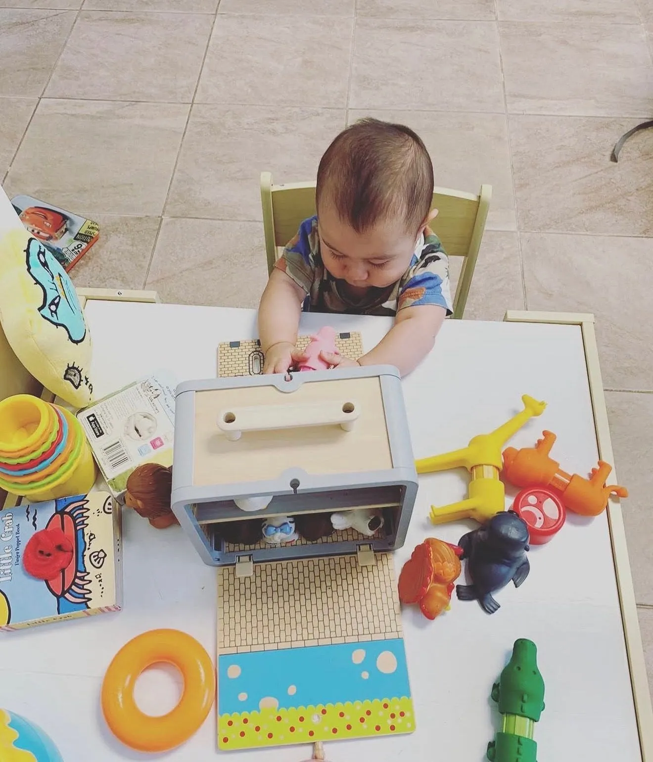 A baby at a low table working through a set of wooden and rubber toys