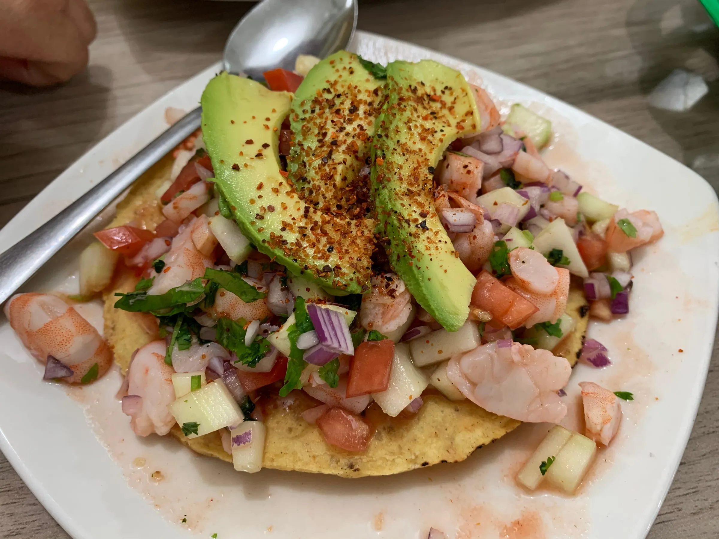 A shrimp ceviche tostada topped with avocado and chilli powder