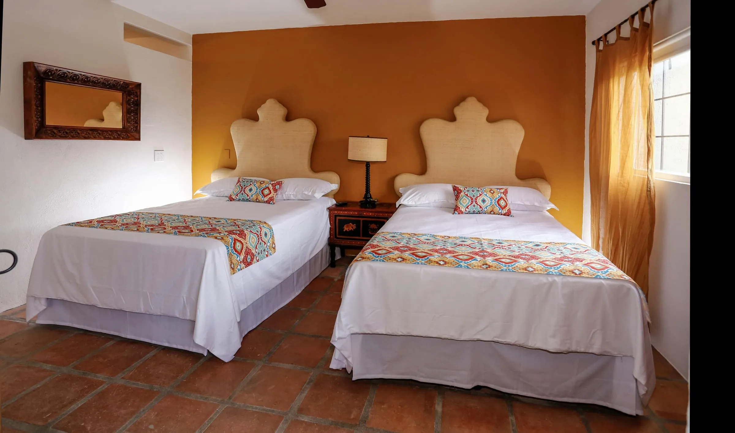 A bedroom with two beds, tiled floor and embroidered covers